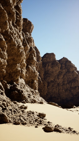 A sandy beach meets a towering rocky cliff in a striking coastal landscape.の写真素材