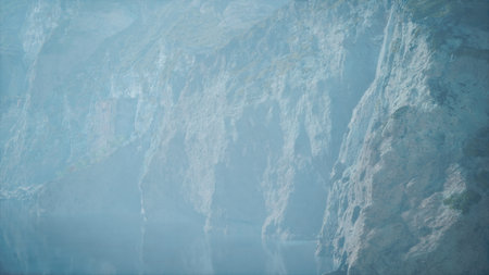 A breathtaking landscape reveals towering cliffs that loom over a tranquil lake. The scene is enveloped in a gentle mist, creating a serene atmosphere perfect for reflection and exploration.の写真素材