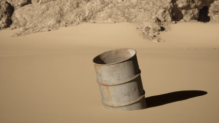 A rusty metal barrel stands partially embedded in fine golden sand at the edge of a desert. The bright sunlight casts a distinct shadow, highlighting the textures of the barrel and surrounding sand.の写真素材