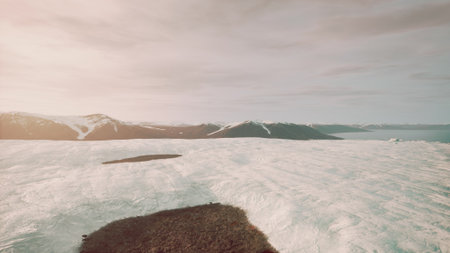 Under a soft evening light, vast white snow blankets the ground while towering mountains rise in the...