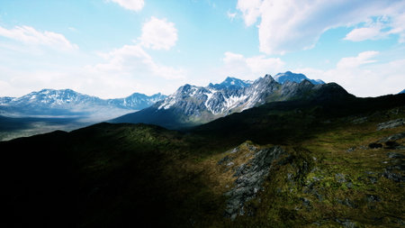 A stunning view of rugged mountain peaks adorned with snow reaches towards a bright blue sky. Lush green valleys cascade beneath, inviting adventure and exploration in natures beauty.の写真素材