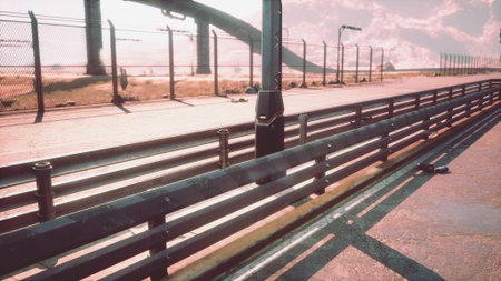 Rusting barriers line the empty racetrack as shadows stretch across the asphalt. The warm glow of the sunset casts an ethereal light, creating a hauntingly beautiful atmosphere.の写真素材