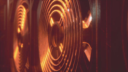 Bright orange lights reflect off the metal grill of a cooling fan, showcasing its intricate design and creating a warm, vibrant atmosphere. The scene conveys a sense of industrial beauty at night.の写真素材