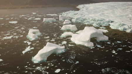 Floating icebergs drift calmly in dark waters as the sun sets behind distant mountains. The tranquility of the Arctic landscape captivates the viewer, showcasing natures beauty.の写真素材