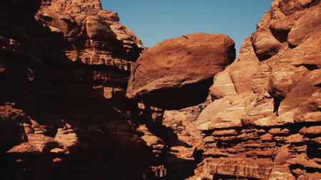 In a stunning natural scene, a large rock sits precariously balanced between two steep canyon walls under a clear blue sky, showcasing the beauty of erosion and geological formations.の写真素材