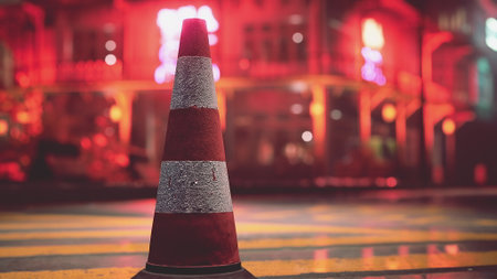 A traffic cone rests on a rain slicked street, illuminated by vibrant neon lights. The surrounding buildings create an atmospheric urban scene, adding a touch of mystery to the night.の写真素材