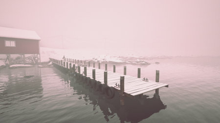 Fog envelops a serene dock as it stretches into calm waters. A simple red cabin stands nearby, enhancing the quiet beauty of the tranquil, misty scene during early dawn.の写真素材