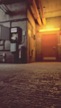 A dimly lit industrial hallway features a vibrant orange glow near a closed door. The textured floor and exposed pipes add depth to this intriguing scene, inviting curiosity about what lies beyond.の写真素材