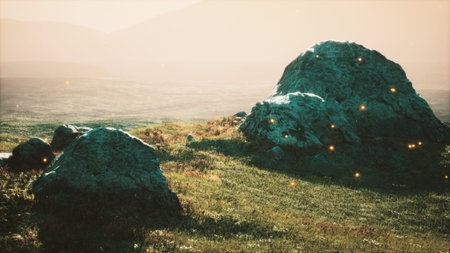 Golden light bathes moss covered rocks amidst gentle grass, creating an enchanting atmosphere. Distant mountains frame the horizon as nature whispers secrets in the twilight.の写真素材