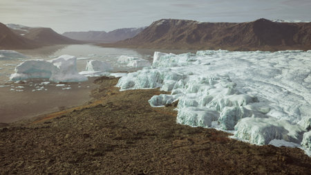 Breathtaking icebergs float gracefully in a tranquil fjord surrounded by towering mountains. The...