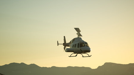 A helicopter ascends into the colorful sky, silhouetted against the grandeur of mountains as the sun sets. The golden light creates a serene atmosphere, showcasing the beauty of nature.の写真素材