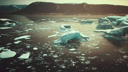 Floating icebergs drift serenely in dark waters under a golden sunset. Majestic mountains form a...