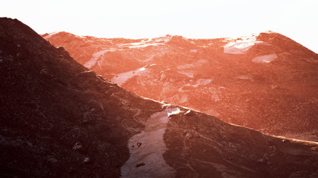 Warm hues sweep across the peaks as the sun sets behind rocky mountains, creating a breathtaking silhouette. The tranquil atmosphere invites contemplation and awe of natures beauty.の写真素材