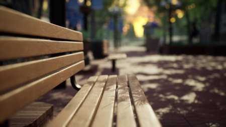 Golden sunlight pours through the lush canopy, casting playful shadows on an empty wooden bench. A peaceful park invites visitors to enjoy natures serenity during late afternoon.の写真素材