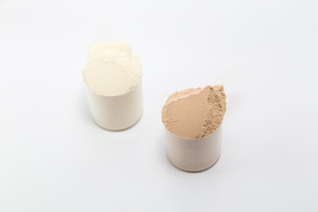 heap of isolate and chocolate protein powder with plastic spoon on white backgroundの写真素材