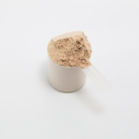 heap of isolate and chocolate protein powder with plastic spoon on white backgroundの写真素材
