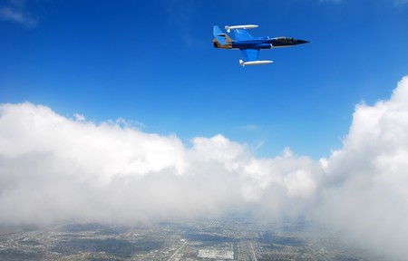 Blue colored fighter jet flying above the clouds                      の写真素材