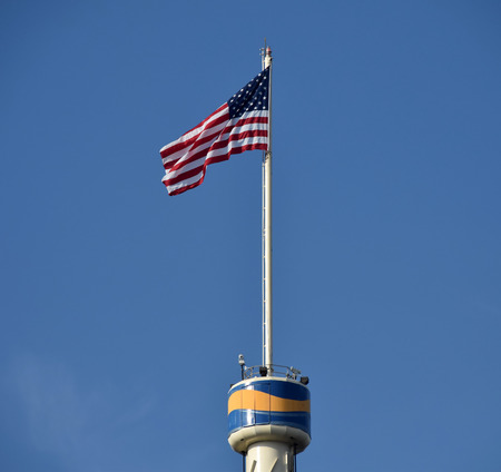 American flag on top of tall tower against blue skyの写真素材