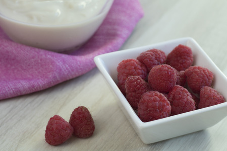 Fresh raspberries in a white jar on a wooden table and soy yogurt on a pink cloth in the background.の写真素材