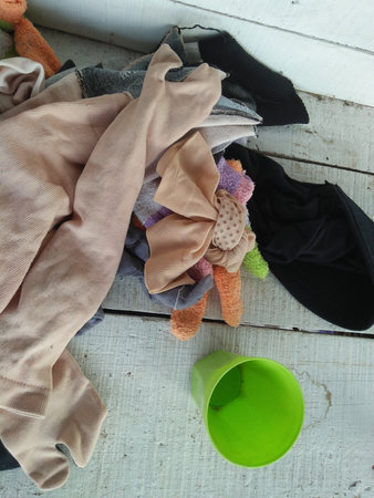 A pile of dirty clothes and a green cup on a wooden floor