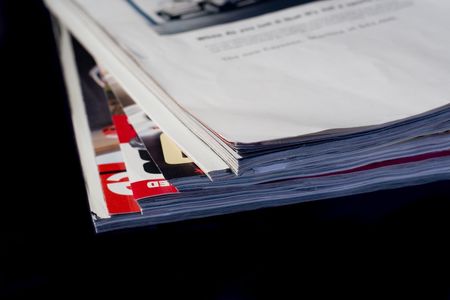 Corner of stack of used magazines isolated on black background