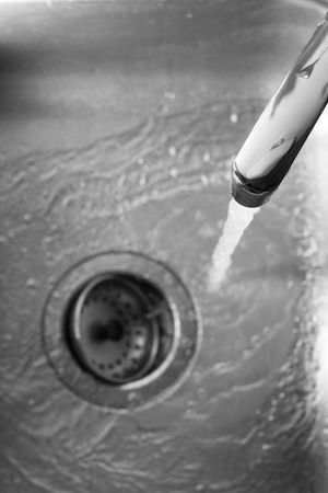 Water pouring from a spout in kitchen sink and flowing down drain 