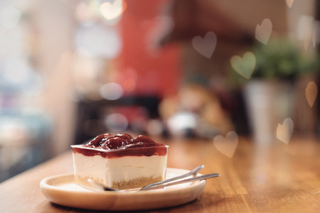 Strawberry cheese cake place on the wooden table with heart bokeh in soft focus and warm fall colorの写真素材