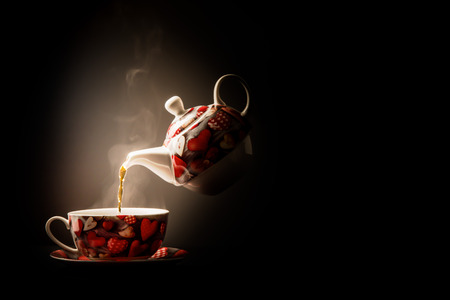 Pouring steaming tea into heart design cup from levitating porcelain teapotの写真素材