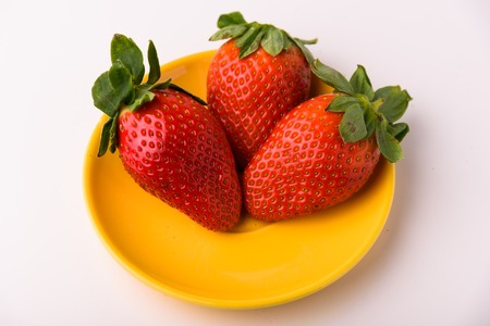Three strawberries on a yellow plate. Isolated on a white backgroundの写真素材