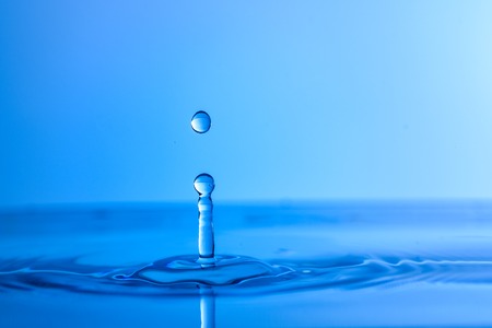 Water drop splash into crystal clear blue water making ripples background