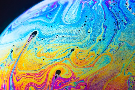 Rainbow soap bubble on a dark background. Close-up of a bubble