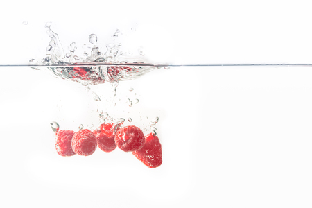 Bunch of juicy delicious looking raspberries splashing into water surface and sinking. Isolated on...