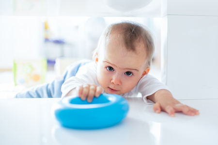Caucasian baby girl squeezing under table to get torus toy, with funny focused expression on her face. Copy space.の写真素材