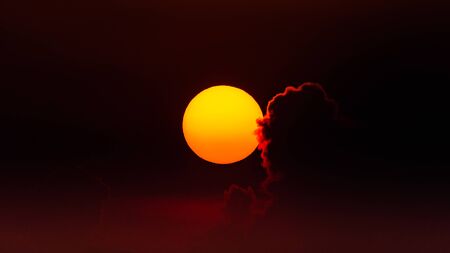 Orange - yellow Sun at sunset against red sky with back lit cloudの写真素材