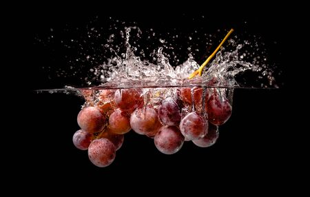 Isolated Red grapes splashing and sinking in water on black backgroundの写真素材