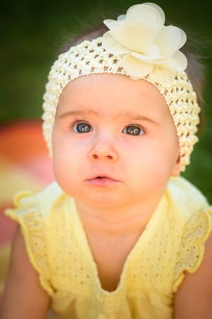 Cute baby girl in yellow band and dress sits in sunny backyard. 8 months old infant outdoors. Development conceptの写真素材