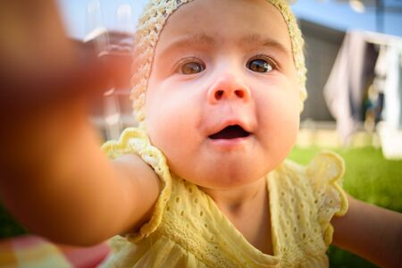 Cute baby girl in yellow reaching camera in sunny day outdoors. Conceptual.の写真素材