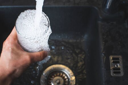 Filling glass of water from stainless steel kitchen faucet. Drinking water concept. Austria pure water from mountains.の写真素材