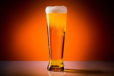 Beer glass with drops on a orange background. Alcohol concept. Copy space.
