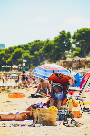 Alcudia, Spain 14.09.2011 - Child covered in sand in stroller on sandy beach sleeping. Kids at summer vacation in sun concept.のeditorial素材