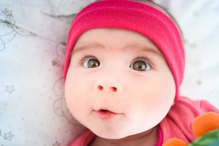 Beautiful portrait of 5 week old baby girl lying in a crib looking up towards camera. Baby care conceptの写真素材