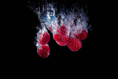 Raspberries falling into a water blackの写真素材