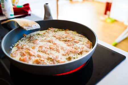 Pan with Cut Salmon Pieces in sour cream with spices on stove. in bright kitchen Healthy food.の写真素材
