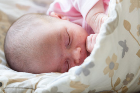 Sleeping newborn baby. Cute little girl one week old at home. Adorable lying on side covered with blanket. No retouch, newborn dry skin.のeditorial素材
