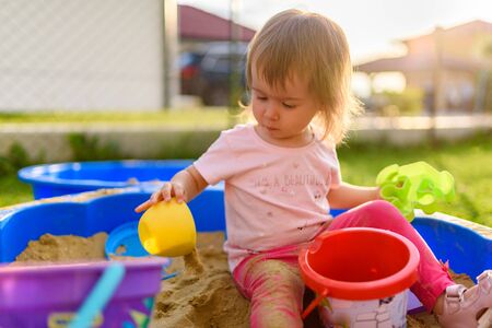 Baby girl playing in a sandbox outdoors in sunny day. Child in blue sandbox in summer.の写真素材