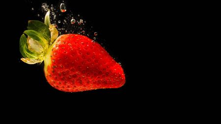 Strawberry falling into water causing bubbles all around it. Healthy food concept. Black backgroundの写真素材