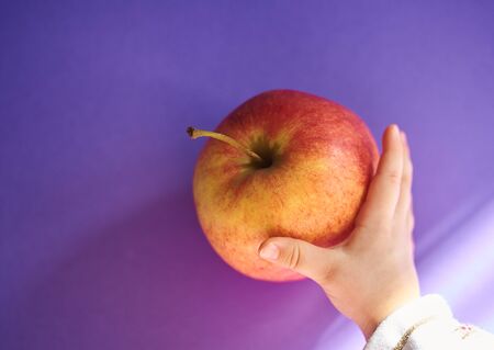 Hand of a baby grabbing an apple from a table. Violet color background. Copy space.の写真素材