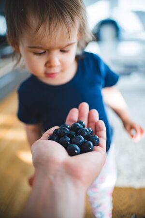 Adorable baby happy to see hand full with blueberries. Portrait of 1 - 2 year old girl. Healthy food...
