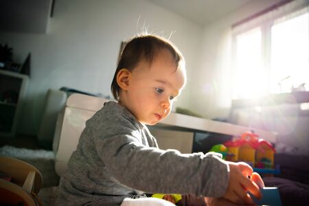 Portrait of one year old baby girl indoors playing on the carpet in bright room playing by herself