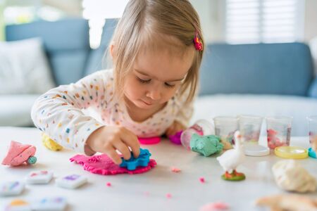 Happy little child, adorable creative 2 year old girl playing with dough plasticine, colorful modeling compound, sitting bright sunny room at home. Education conceptの写真素材